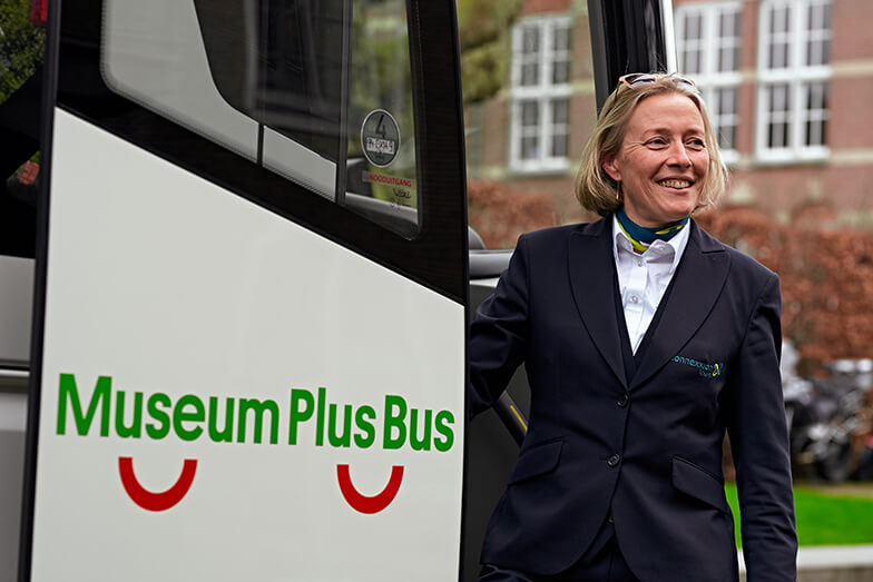 De chauffeur staat lachend in de deuropening van de Museum Plus Bus