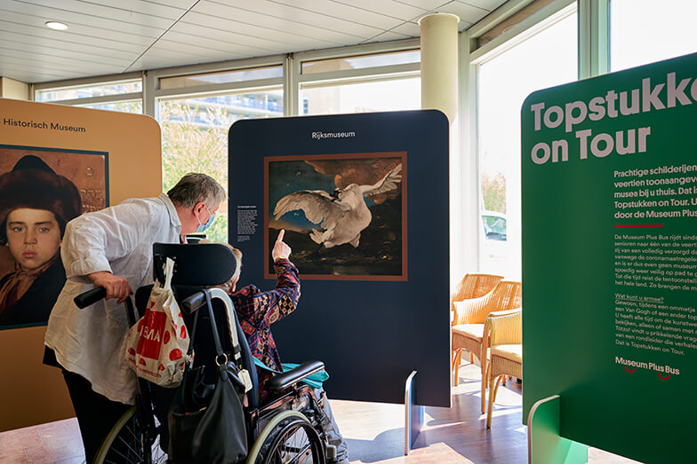 Een dame in rolstoel kijkt samen met haar begeleider naar een replica uit het Rijksmuseum